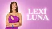 Lexi Luna pose devant un stand promotionnel lors d'un salon professionnel. Elle porte une robe moulante violette à découpe asymétrique et croise les bras en regardant l'objectif, avec en arrière-plan une affiche à son effigie sur fond rose.
