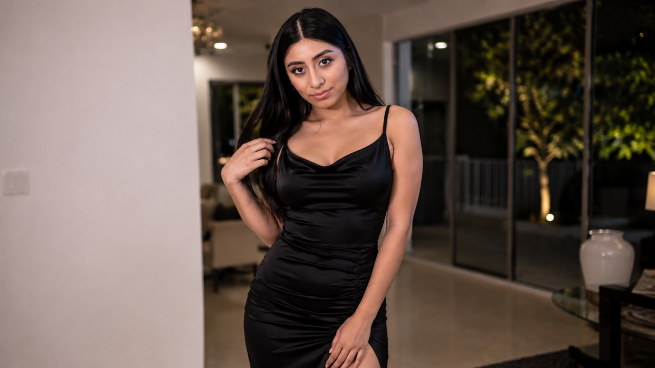 Violet Myers porte une robe noire ajustée et pose dans une pièce lumineuse au décor contemporain.